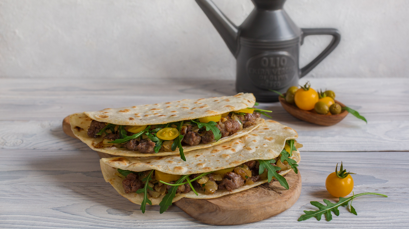 Two piadine folded over a filling of meat, cherry tomatoes and arugula, on a wooden board